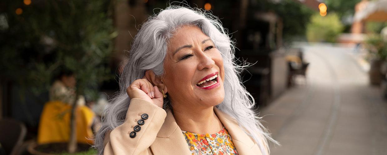 Donna che sorride e preme il pulsante sui suoi apparecchi acustici 