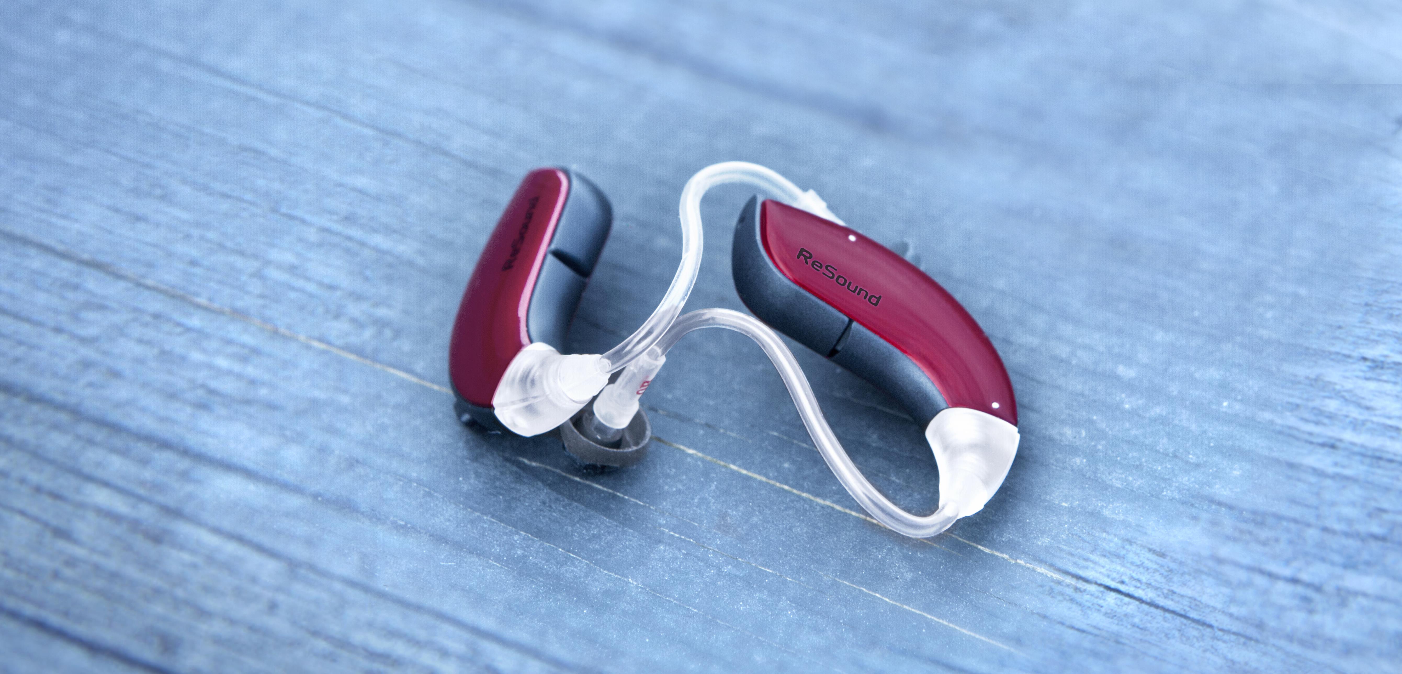 Pair of ReSound red hearing aids on a table. 